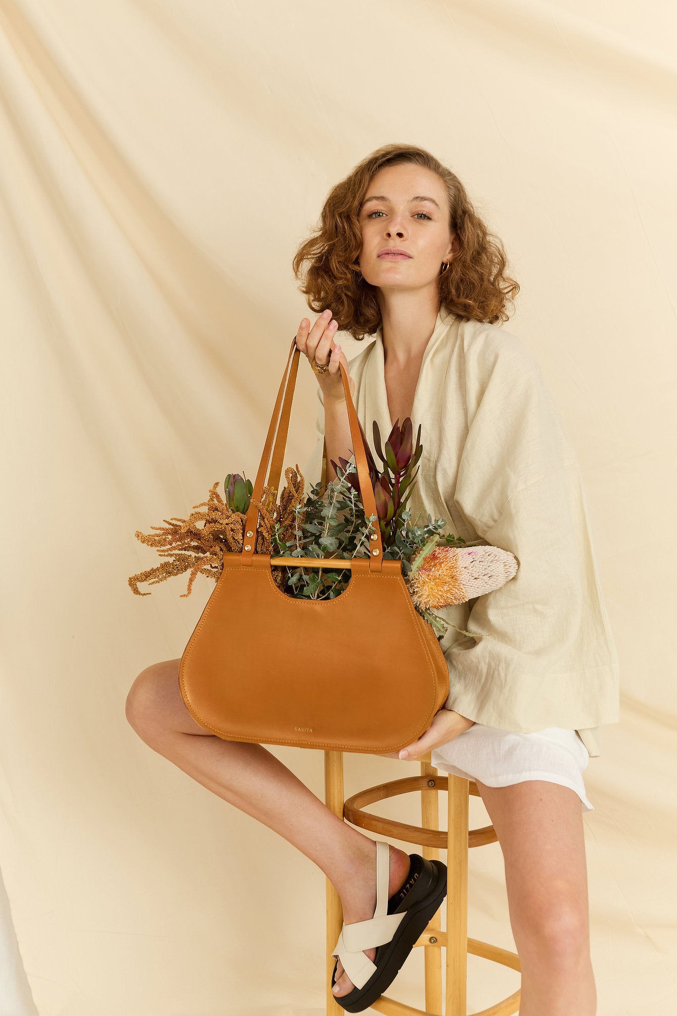 Model holding the Ophelia tote leather bag in tan with flowers inside