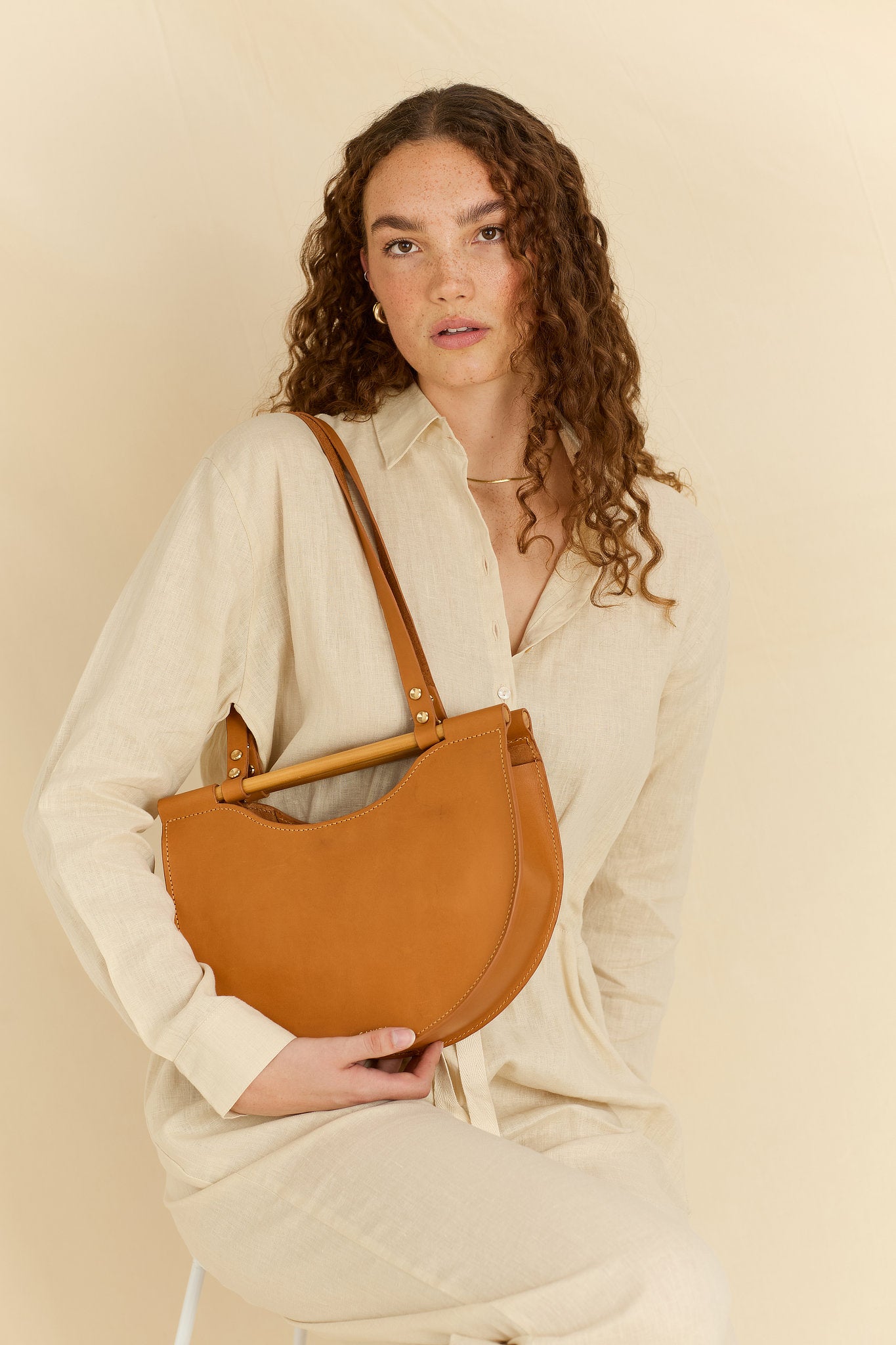 Model facing forward wearing the Celine half moon leather shoulder bag in tan