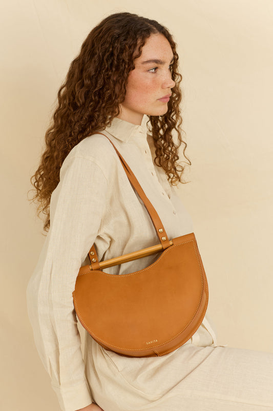 Model facing sideways wearing the Celine half moon leather shoulder bag in tan