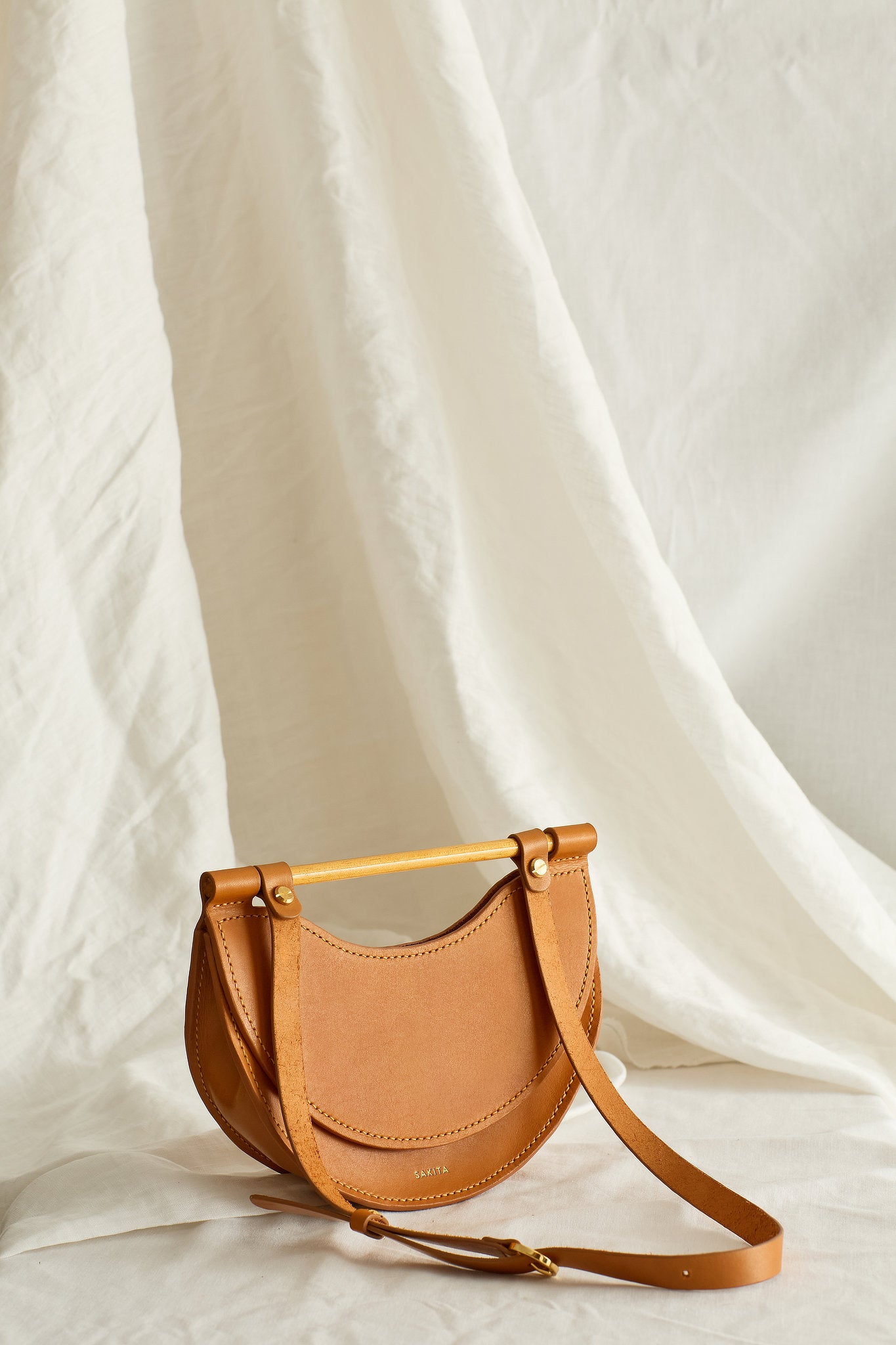 Angled view of the Elodie mini half-moon leather shoulder bag in tan colour