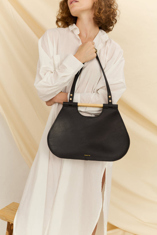 Model faced forward holding the Ophelia black leather tote bag in front of her