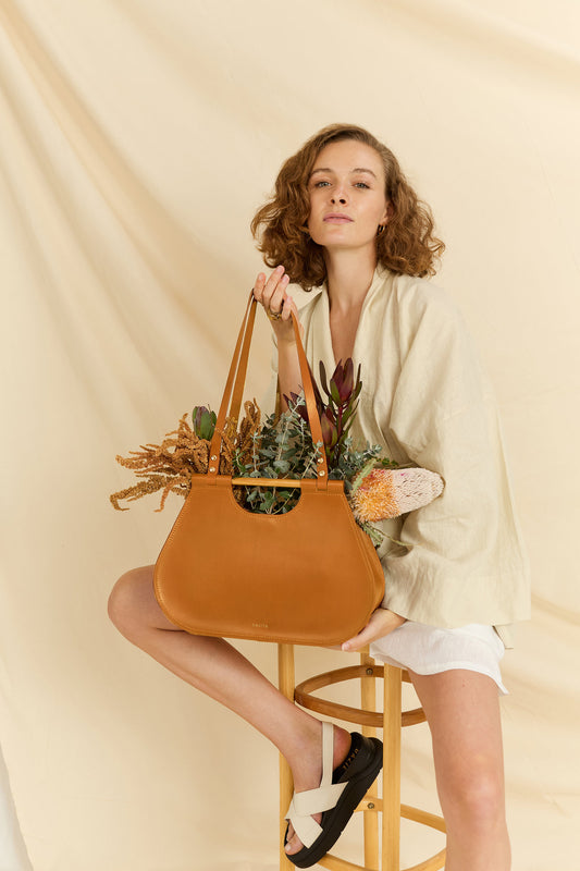 Model holding the Ophelia tote leather bag in tan with flowers inside 