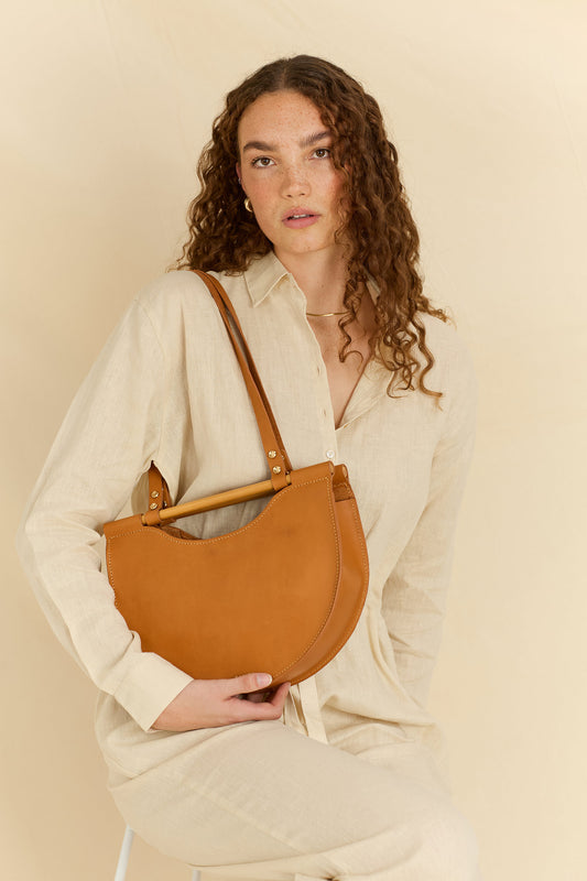 Model facing forward wearing the Celine half moon leather shoulder bag in tan
